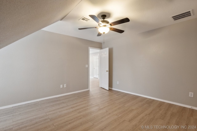 spare room with ceiling fan, vaulted ceiling, a textured ceiling, and light hardwood / wood-style flooring