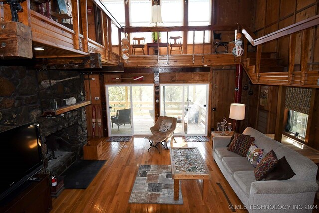 living room featuring wood walls, wood-type flooring, a towering ceiling, and a stone fireplace