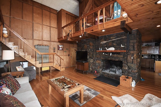 living room featuring hardwood / wood-style flooring, high vaulted ceiling, wooden walls, and a stone fireplace