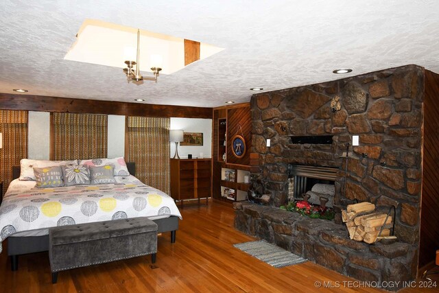 bedroom with a stone fireplace, a textured ceiling, and hardwood / wood-style flooring