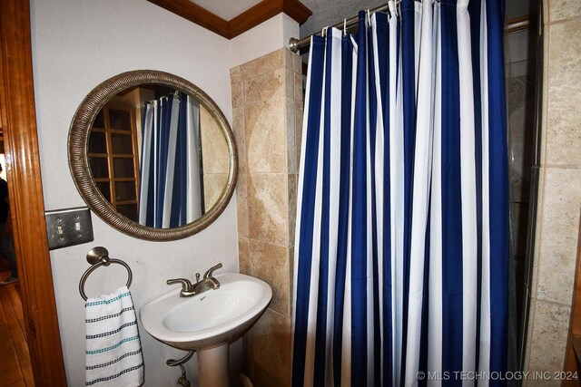 bathroom featuring walk in shower, sink, tile walls, and ornamental molding