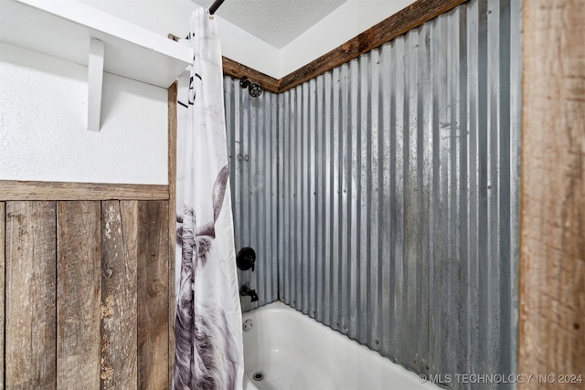 bathroom with a textured ceiling and shower / bathtub combination with curtain