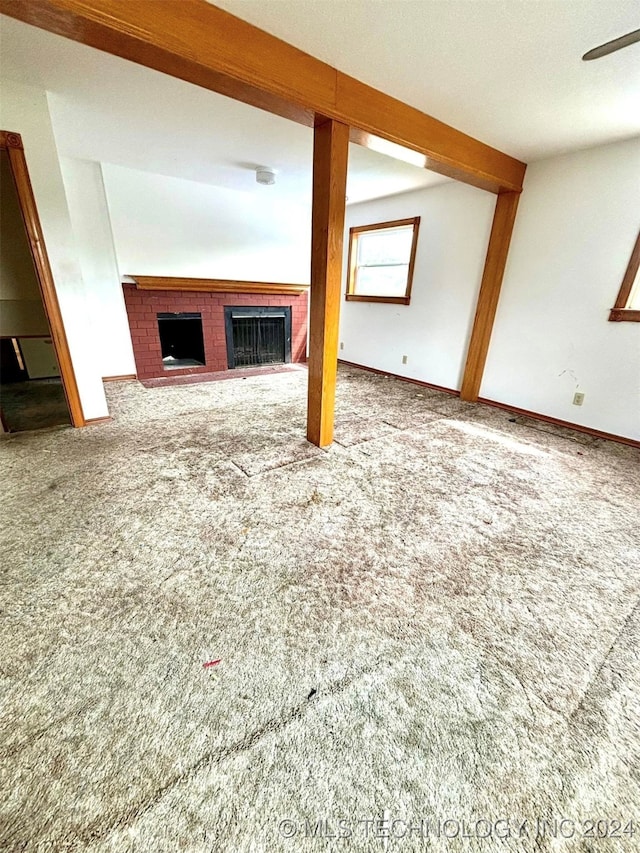 unfurnished living room with carpet floors, beamed ceiling, and a tiled fireplace