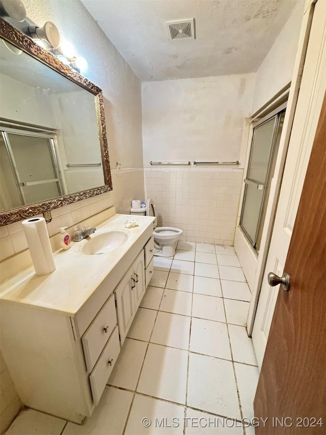 bathroom with a shower with door, toilet, vanity, and tile walls