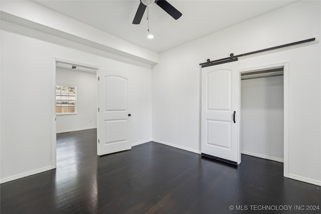 unfurnished bedroom featuring ceiling fan, a barn door, a closet, and dark hardwood / wood-style floors