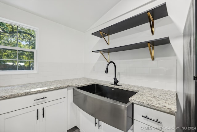 kitchen featuring lofted ceiling, light stone countertops, white cabinets, and sink