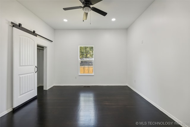 unfurnished bedroom with ceiling fan, a barn door, and dark hardwood / wood-style flooring