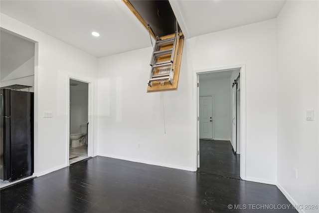 empty room with a barn door and dark wood-type flooring