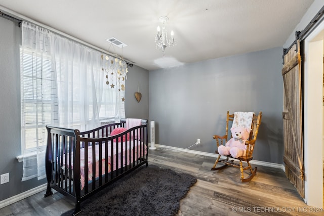 bedroom featuring multiple windows, a nursery area, a barn door, and hardwood / wood-style floors