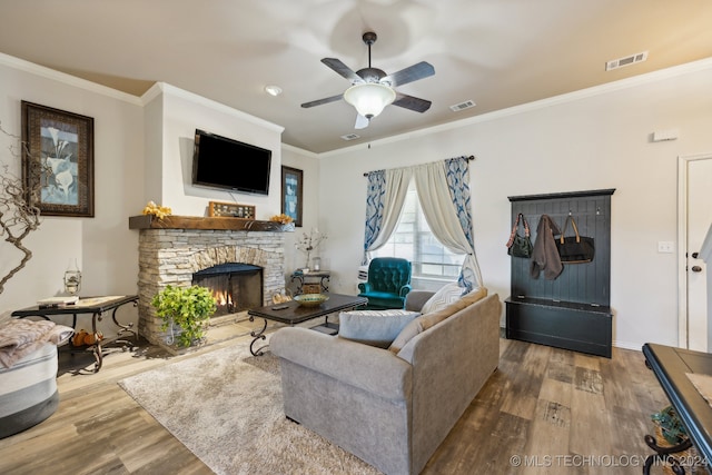 living room with hardwood / wood-style floors, a stone fireplace, crown molding, and ceiling fan