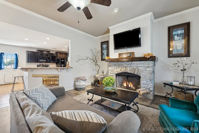 living room featuring light hardwood / wood-style floors, ornamental molding, a stone fireplace, and ceiling fan