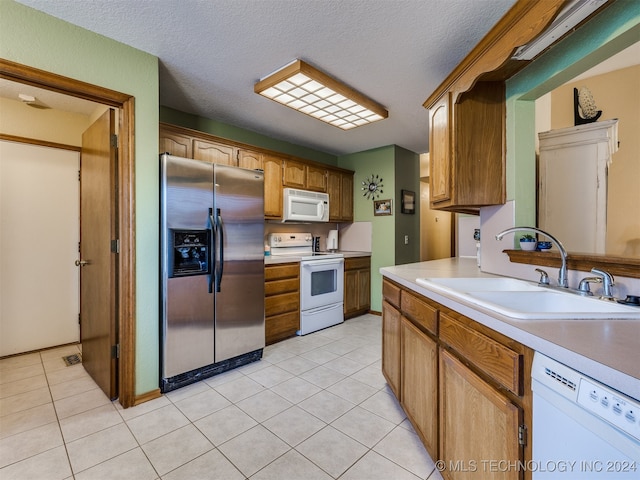 kitchen with light tile patterned flooring, white appliances, sink, and a textured ceiling