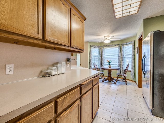 kitchen with ceiling fan, stainless steel fridge, sink, light tile patterned flooring, and a textured ceiling