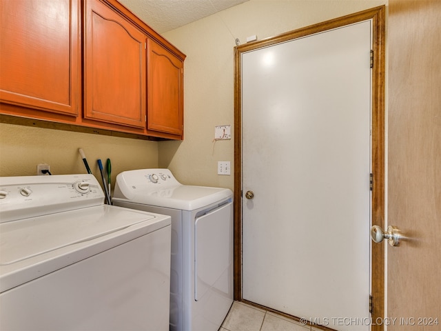 clothes washing area with a textured ceiling, washer and dryer, light tile patterned floors, and cabinets