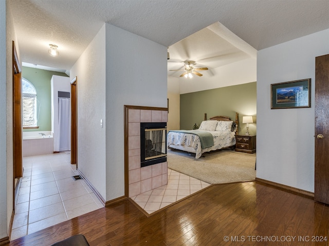 bedroom with ceiling fan, a textured ceiling, a fireplace, ensuite bath, and light hardwood / wood-style floors