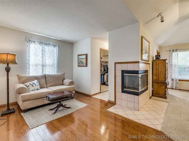 living room featuring vaulted ceiling, a textured ceiling, a fireplace, and light hardwood / wood-style floors