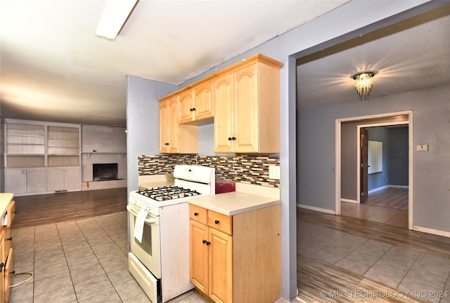 kitchen with backsplash, light wood-type flooring, white gas range, light brown cabinets, and a brick fireplace