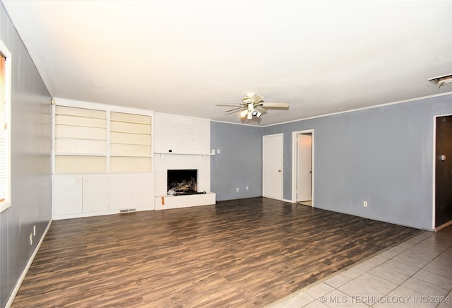 unfurnished living room with built in shelves, wood-type flooring, ceiling fan, and a fireplace