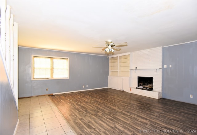 unfurnished living room featuring a brick fireplace, hardwood / wood-style flooring, built in features, and ceiling fan