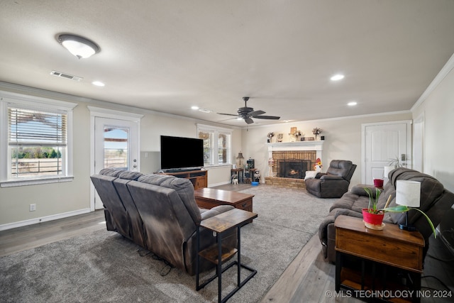 living room with hardwood / wood-style flooring, ceiling fan, ornamental molding, a fireplace, and a healthy amount of sunlight