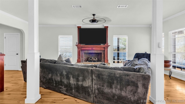 living room featuring a fireplace, crown molding, light wood-type flooring, and a healthy amount of sunlight