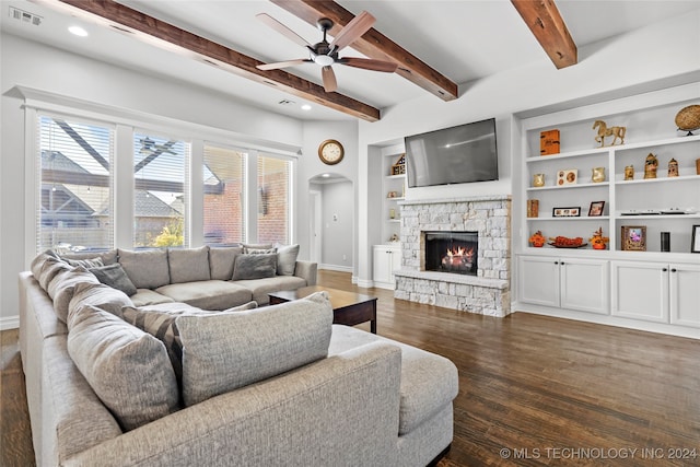 living room with beam ceiling, ceiling fan, dark wood-type flooring, a fireplace, and built in shelves