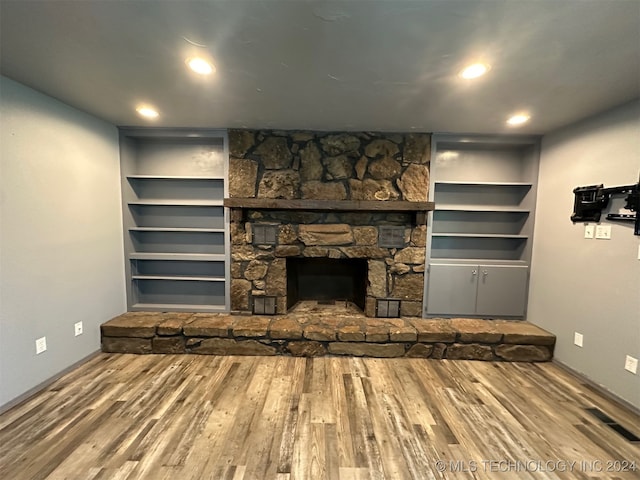 unfurnished living room with wood-type flooring, a stone fireplace, and built in shelves