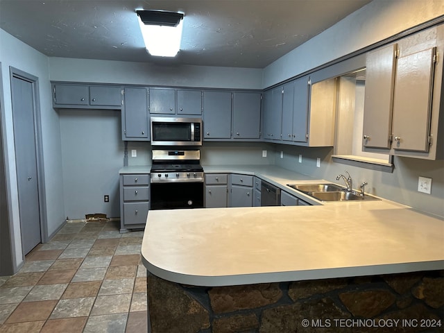 kitchen featuring appliances with stainless steel finishes, sink, kitchen peninsula, and gray cabinetry