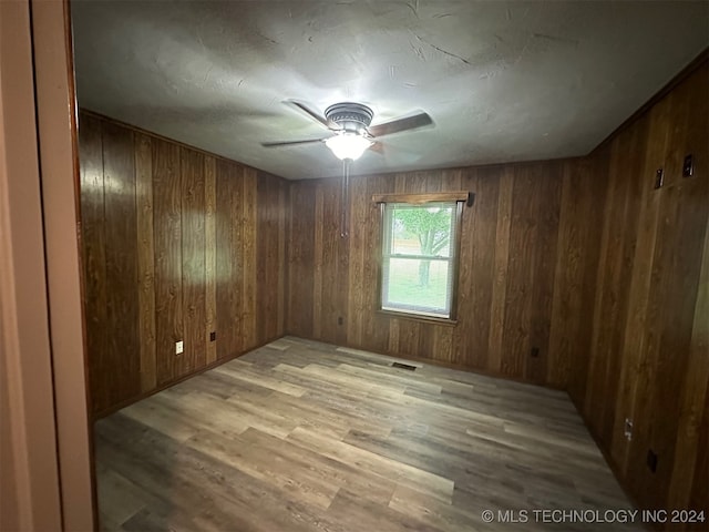 spare room with wooden walls, light wood-type flooring, and ceiling fan