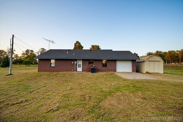 rear view of house featuring central air condition unit, a garage, a storage shed, and a lawn