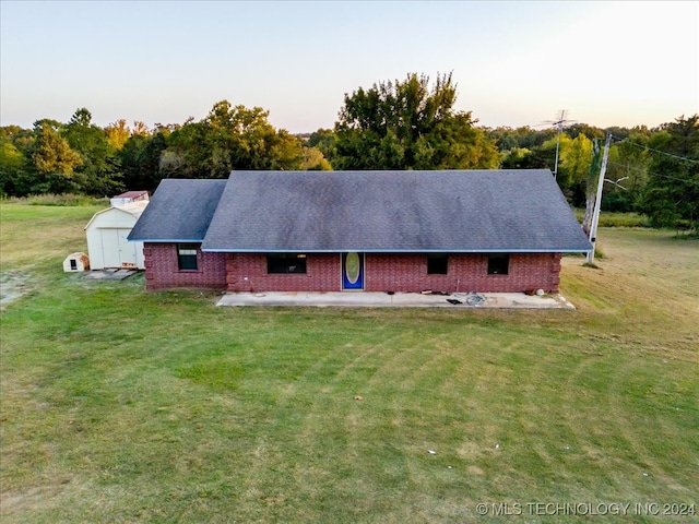 back house at dusk featuring a yard, a patio, and a storage shed