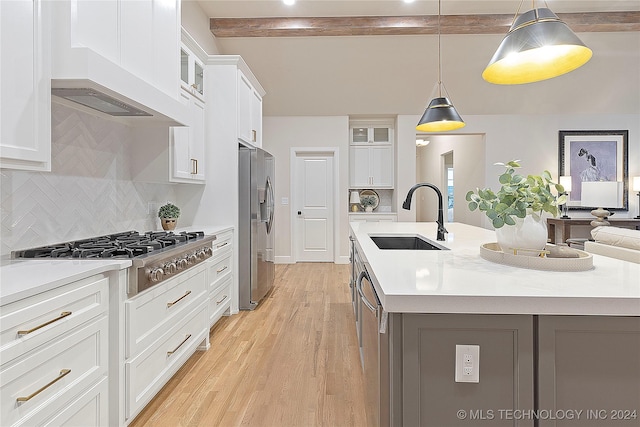 kitchen with stainless steel appliances, a sink, light countertops, light wood finished floors, and a center island with sink