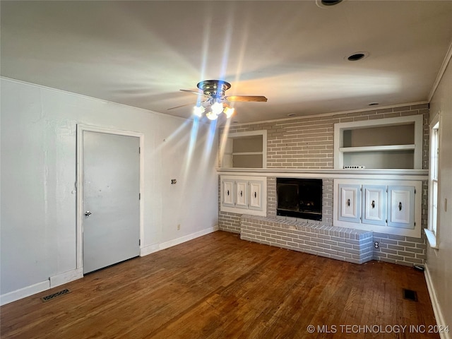 unfurnished living room featuring built in shelves, crown molding, a fireplace, hardwood / wood-style flooring, and ceiling fan