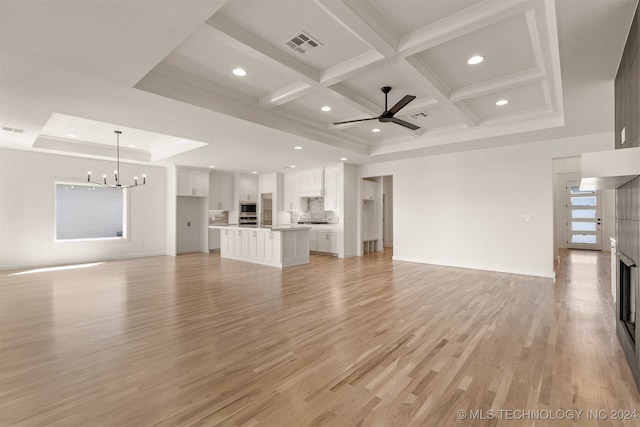 unfurnished living room featuring ceiling fan with notable chandelier, beam ceiling, coffered ceiling, and light hardwood / wood-style flooring