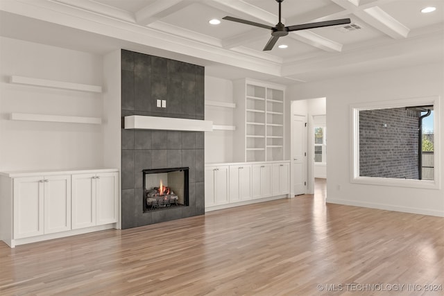 unfurnished living room featuring ceiling fan, coffered ceiling, a tiled fireplace, light hardwood / wood-style flooring, and beam ceiling