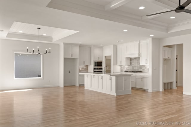 kitchen with light countertops, stainless steel microwave, a kitchen island with sink, and white cabinets