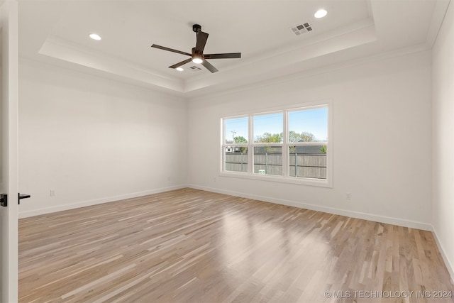 spare room featuring ornamental molding, a tray ceiling, light wood-type flooring, and ceiling fan