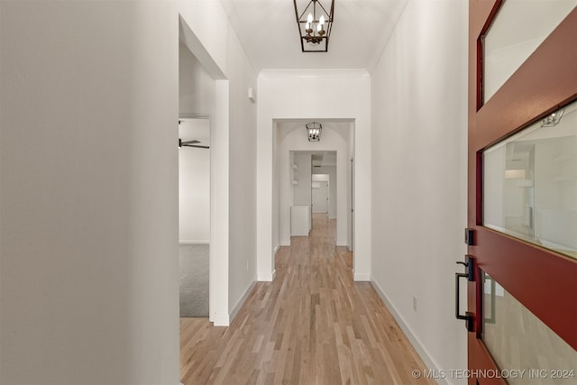 hall with a chandelier, ornamental molding, light wood-style flooring, and baseboards