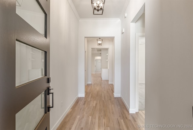 hall featuring light wood finished floors, baseboards, ornamental molding, and a chandelier