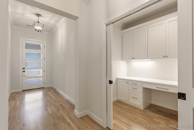 interior space with light hardwood / wood-style floors, crown molding, a chandelier, and built in desk