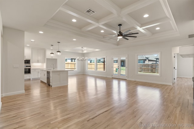 unfurnished living room with ceiling fan with notable chandelier, coffered ceiling, light hardwood / wood-style flooring, and a wealth of natural light