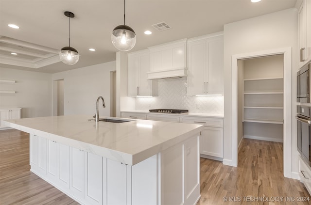 kitchen with a center island with sink, light wood-type flooring, sink, and white cabinets