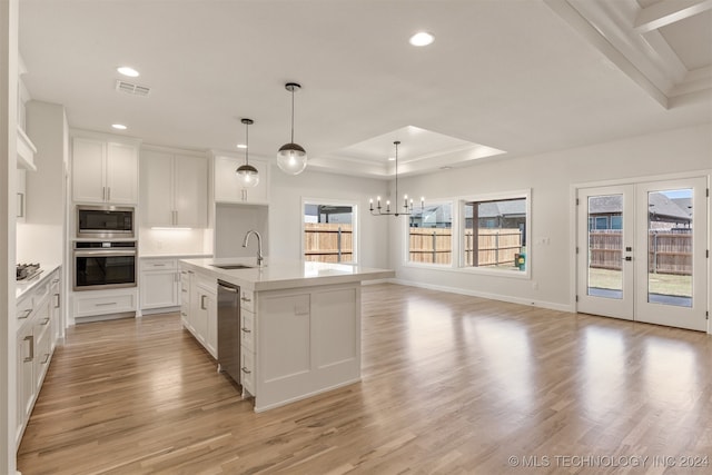 kitchen featuring light countertops, appliances with stainless steel finishes, a center island with sink, and white cabinetry