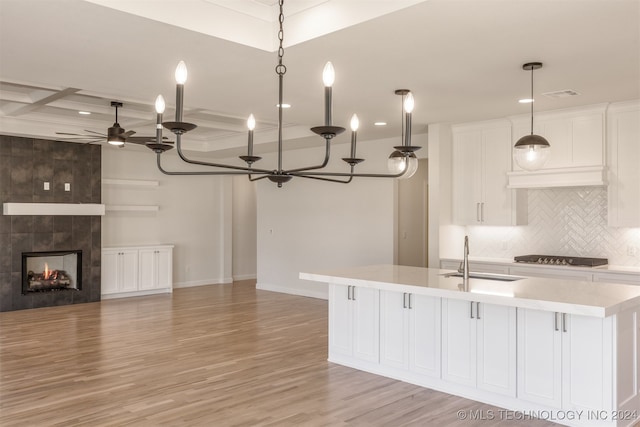 kitchen featuring light wood-type flooring, a center island with sink, sink, hanging light fixtures, and white cabinetry