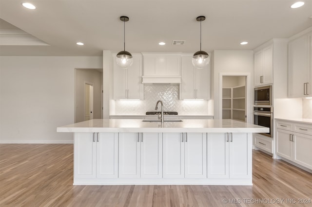 kitchen featuring a kitchen island with sink, stainless steel appliances, light wood-type flooring, and white cabinetry