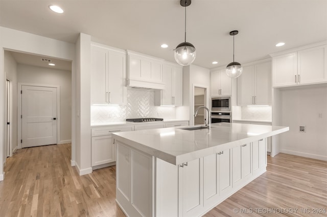 kitchen featuring stainless steel appliances, white cabinets, a sink, and an island with sink