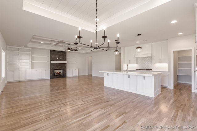 kitchen featuring a kitchen island with sink, white cabinets, pendant lighting, a tray ceiling, and light hardwood / wood-style flooring