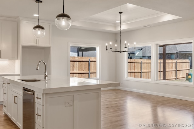 kitchen featuring a sink, white cabinetry, a raised ceiling, a center island with sink, and pendant lighting