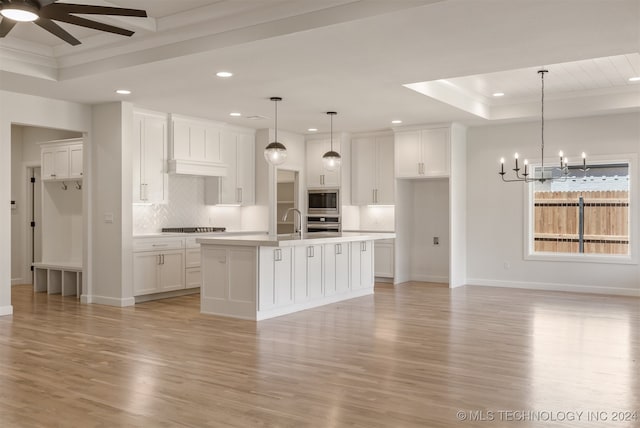 kitchen with white cabinets, a kitchen island with sink, a tray ceiling, and light hardwood / wood-style flooring