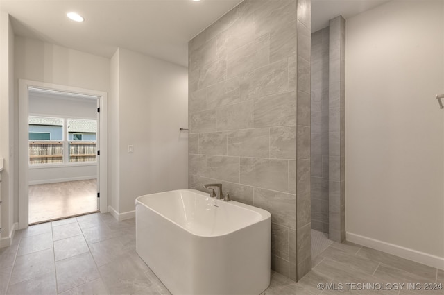 bathroom with baseboards, tile patterned flooring, a freestanding tub, tile walls, and recessed lighting